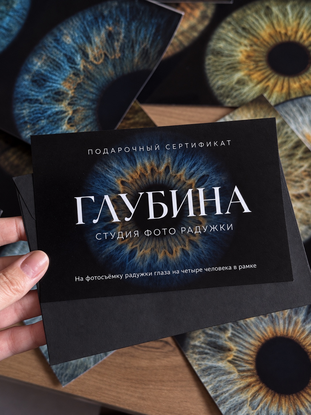 Подарочный сертификат студии ГЛУБИНА в руках на фоне фотографий радужек